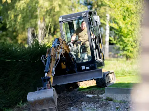 Minibagger bei Erdarbeiten an einer Hecke